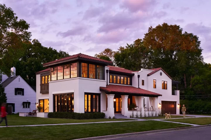 Mediterranean style custom home in St Paul with white exterior, red tile roof, and warm interior lighting at dusk.
