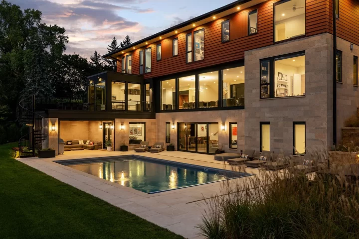 Twilight view of a modern custom home in Mendota Heights with large windows, poolside patio, and architectural lighting